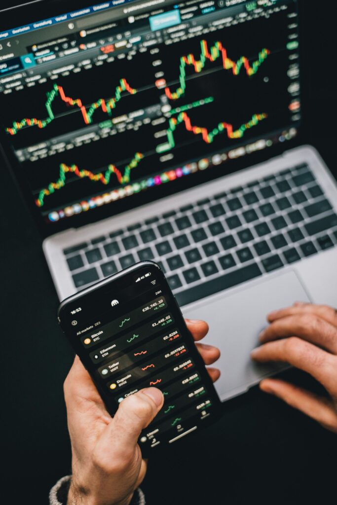 Person analyzing stock market data with a laptop and smartphone showing trading graphs.